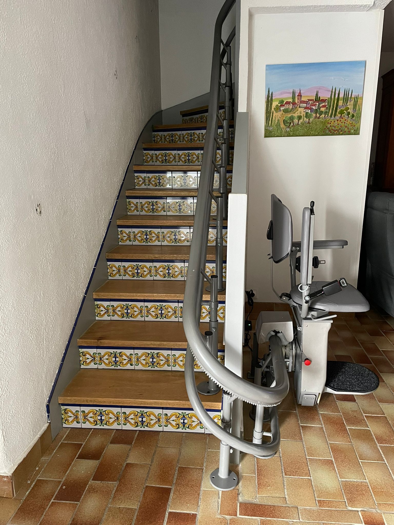 Monte-escalier intérieur incurvé à côté d'un escalier aux marches carrelées à motifs et d'un tableau mural encadré