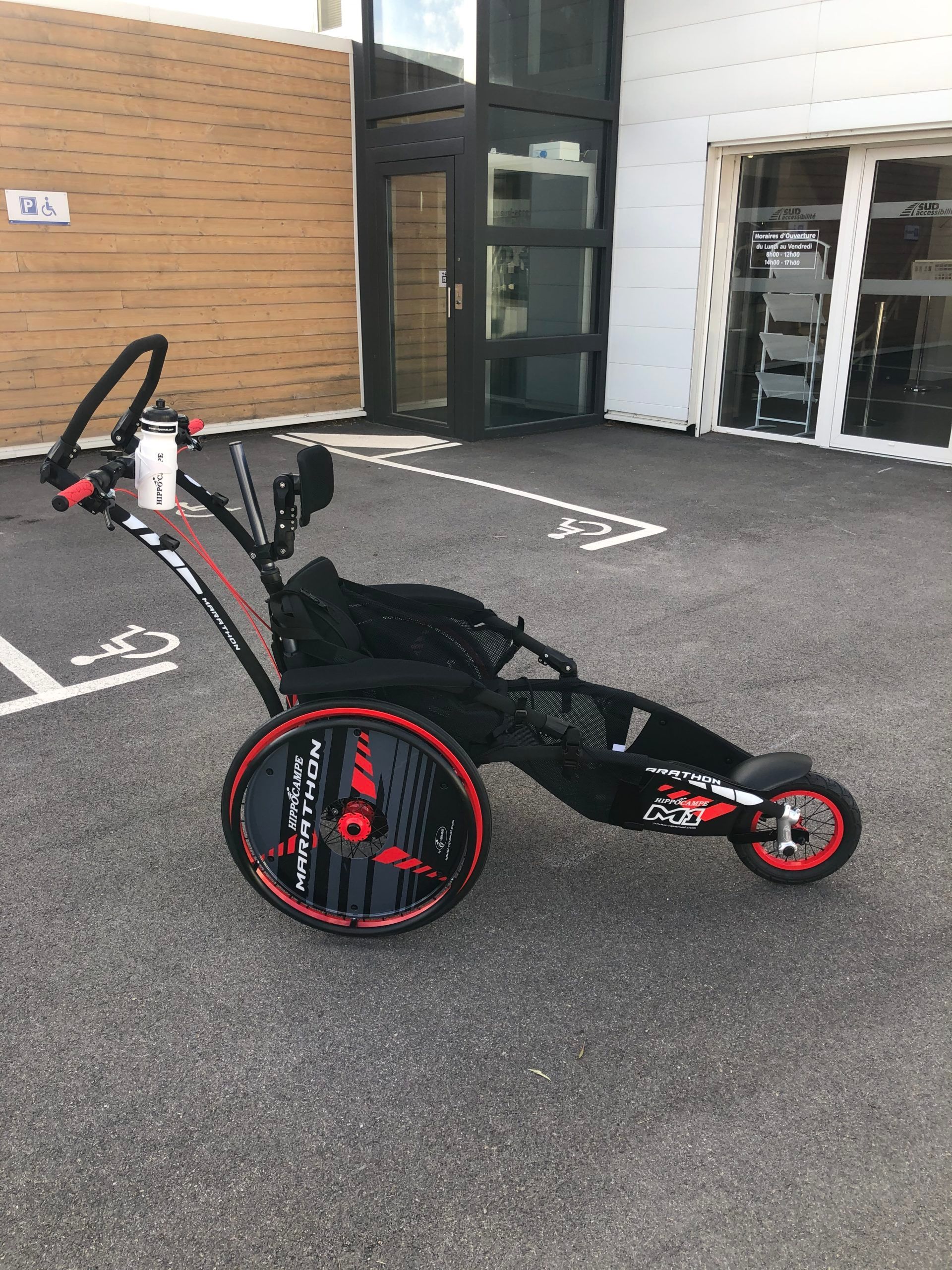 Dispositif d'aide pour les PMR sur un parking asphalté devant un bâtiment.
