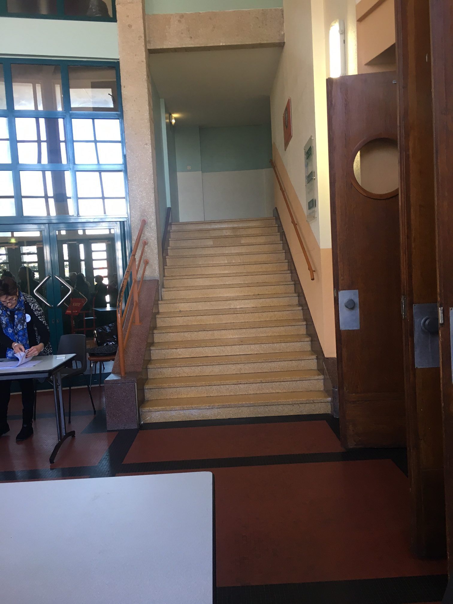 Escalier dans un couloir avec une personne assise à une table à gauche et une porte en bois à droite