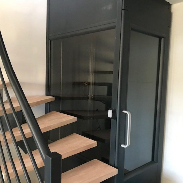 Un ascenseur noir à côté d'un escalier en bois ; porte entrouverte.