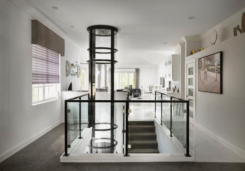 Intérieur avec ascenseur privatif, cage d'escalier, garde-corps en verre et murs blancs.