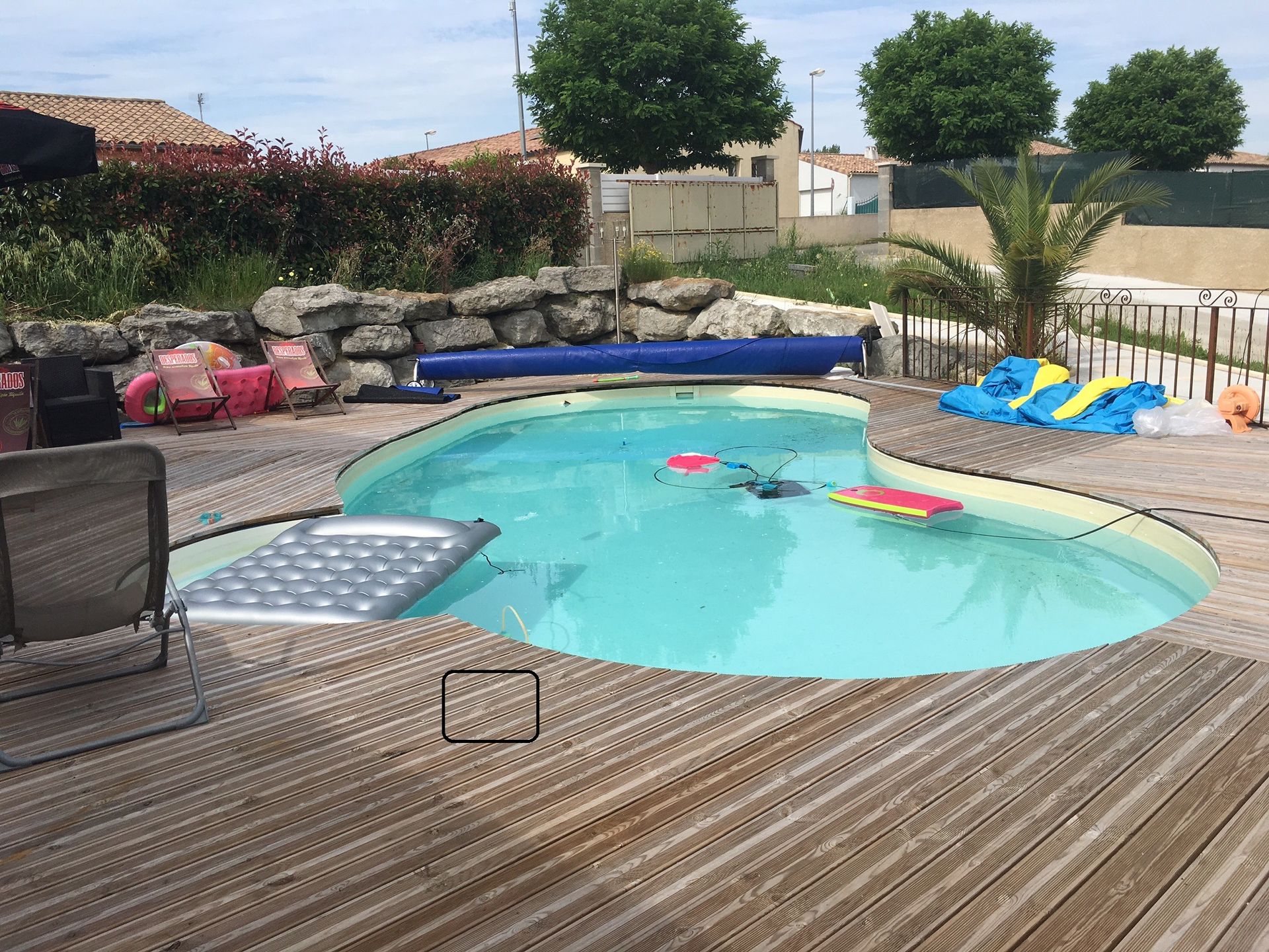 Piscine dans le jardin avec eau turquoise, terrasse en bois, chaises longues et bouées colorées