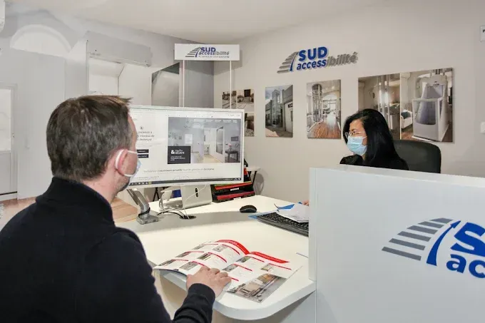 Deux personnes dans le bureau de Sud Accessibilité, avec des brochures et des présentoirs de produits.