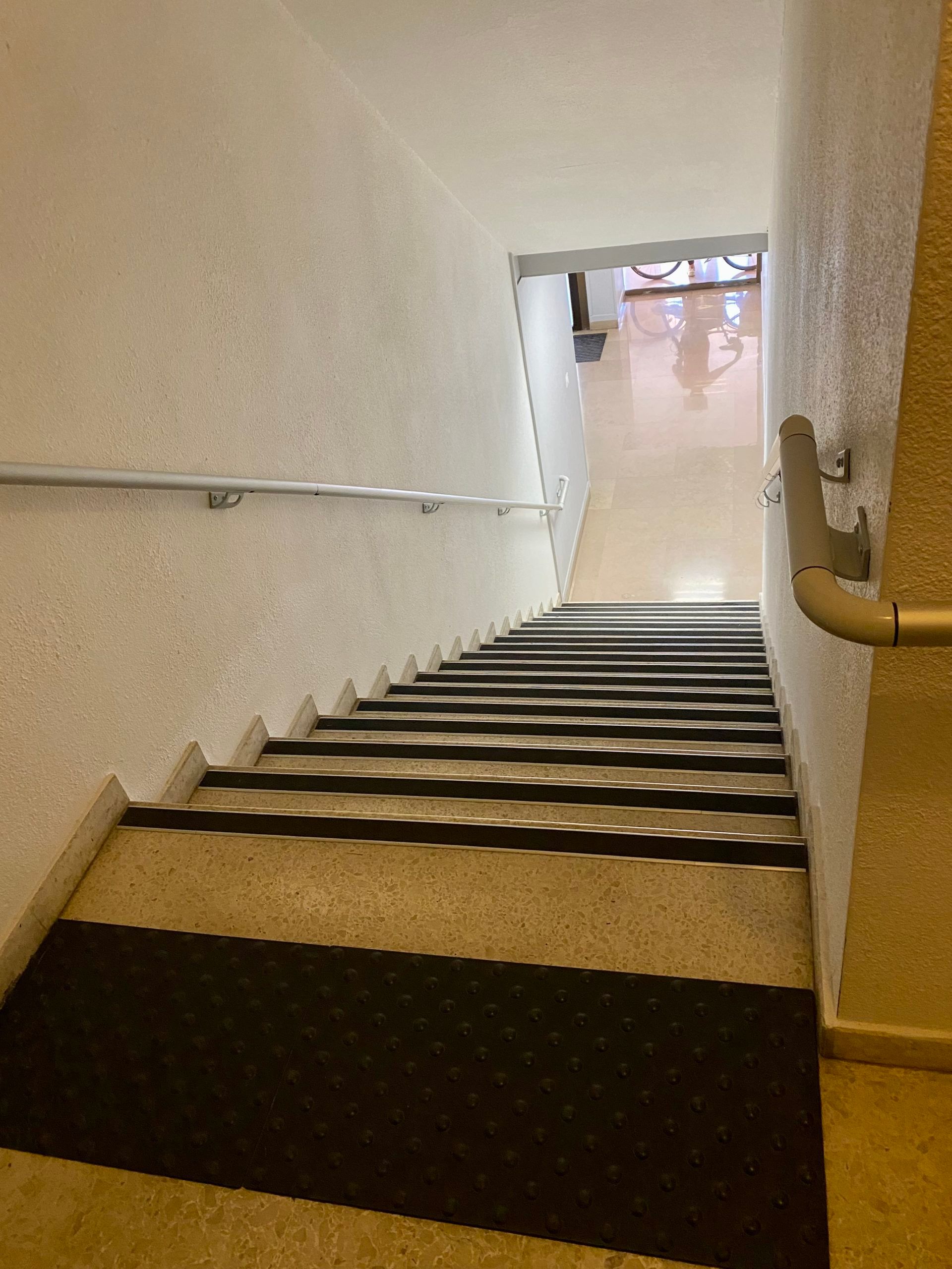 Escalier avec rampes descendant vers un palier clair. Les marches ont une surface texturée noire.