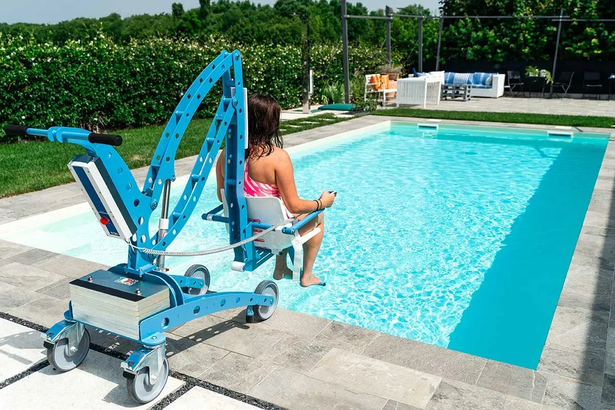 Une femme utilise un élévateur de piscine bleu pour entrer dans une piscine turquoise. L'élévateur se trouve sur une terrasse extérieure.