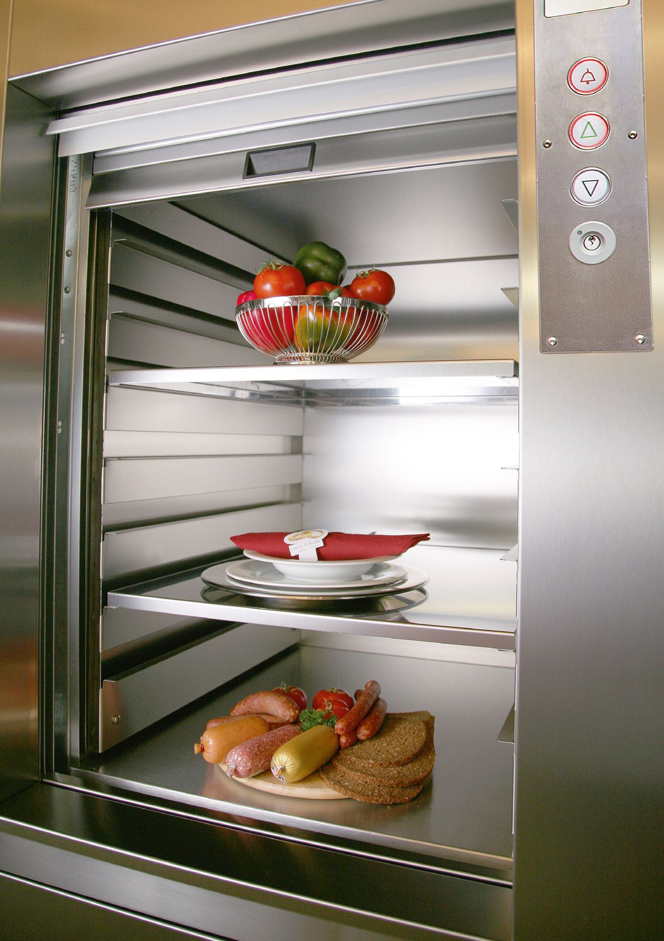 Un monte-charge avec des aliments sur des étagères : des légumes, une assiette avec une serviette.
