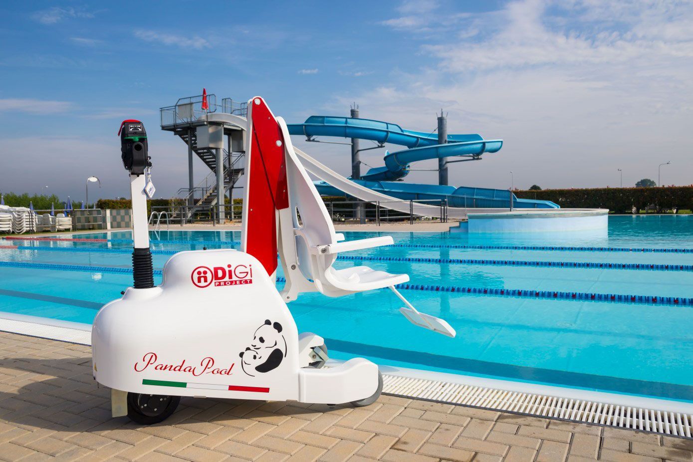 Un dispositif d'accès au bain pour piscine blanc, près des toboggans aquatiques bleus et d'une piscine dans un parc aquatique.