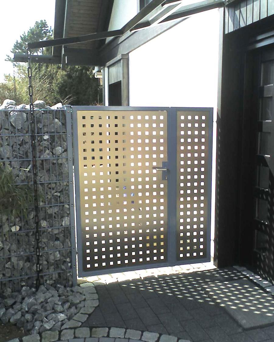 Ein Metalltor mit Löchern darin steht vor einer Steinmauer