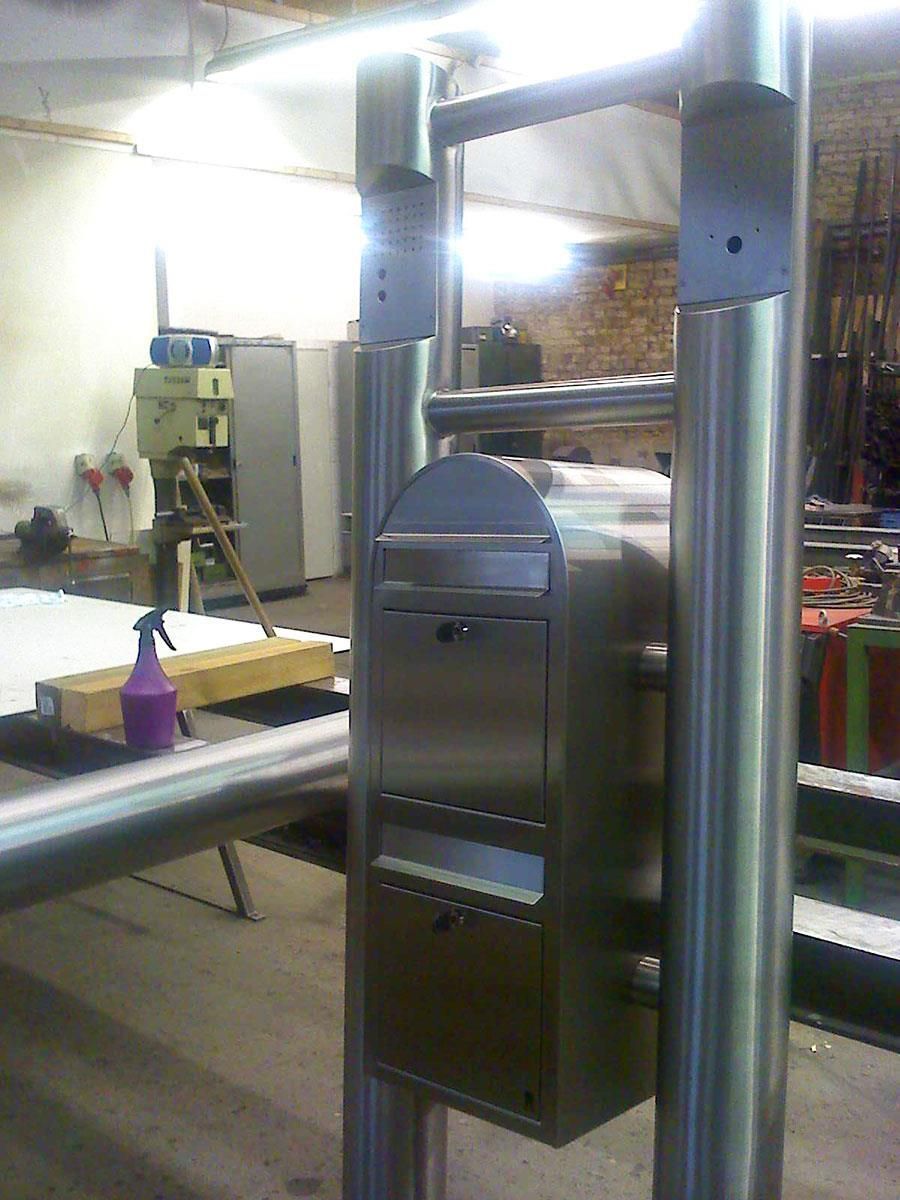 In einem Raum steht auf einer Metallstange ein Briefkasten aus Edelstahl.