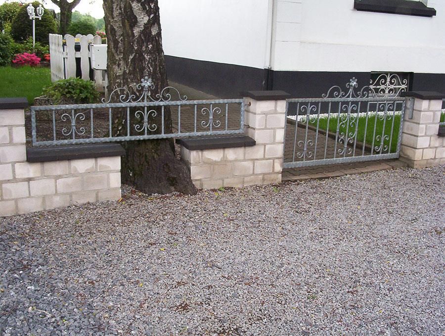 Eine Backsteinmauer mit einem Metalltor vor einem Haus