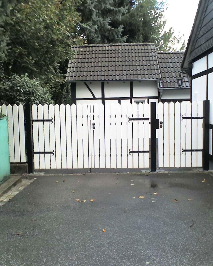 Ein weißer Lattenzaun umgibt eine Einfahrt vor einem Haus