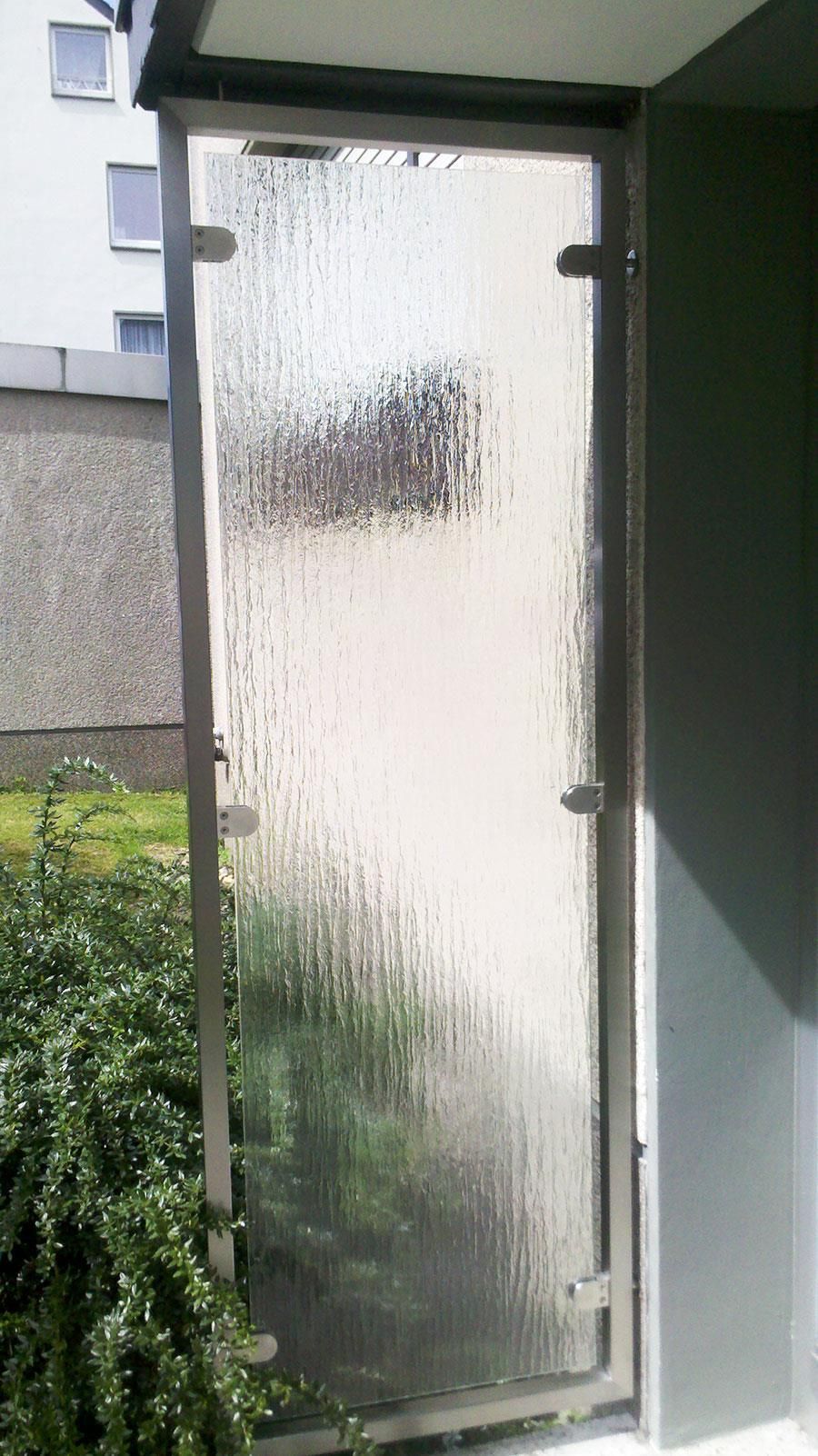 An der Seite eines Gebäudes neben einem Busch befindet sich eine Glastür.