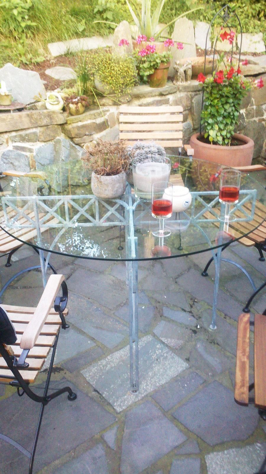 Ein Glastisch mit zwei Gläsern Wein darauf auf einer Terrasse.