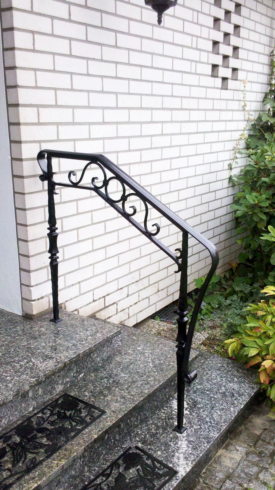 An der Seite eines weißen Backsteingebäudes ist ein schmiedeeisernes Geländer angebracht.