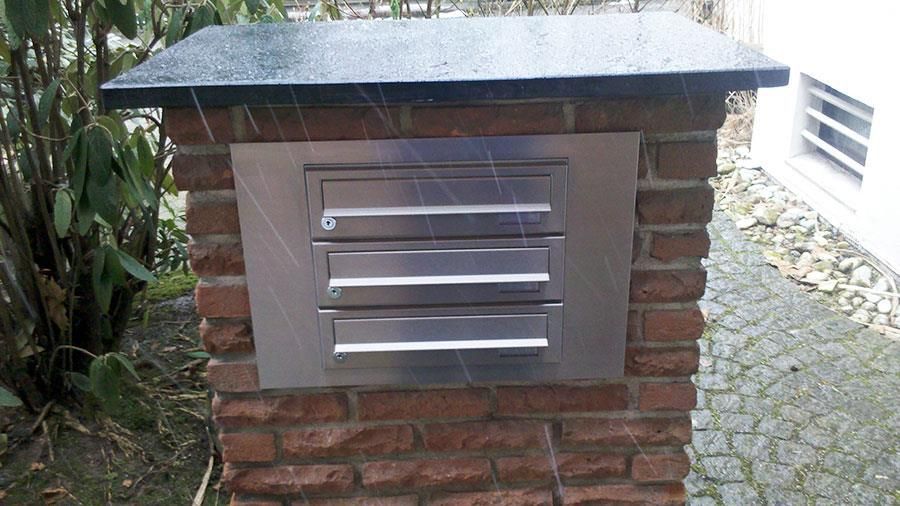 Ein Briefkasten aus Edelstahl ist in eine Ziegelwand eingebaut.