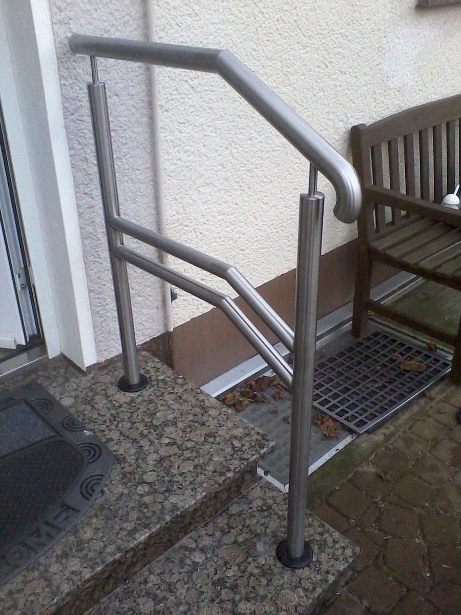 Ein Edelstahlgeländer an einer Treppe neben einer Holzbank.