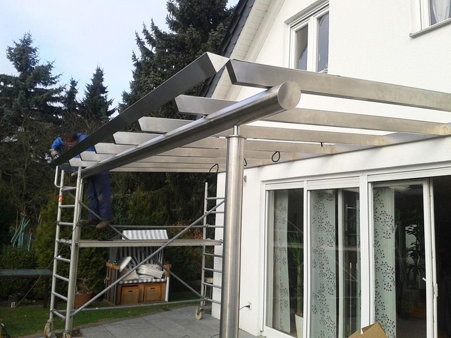 Ein Mann auf einer Leiter arbeitet an einer Pergola vor einem Haus