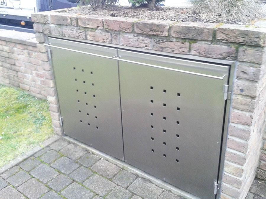 An einer Ziegelwand ist ein Mülleimer aus Edelstahl befestigt.