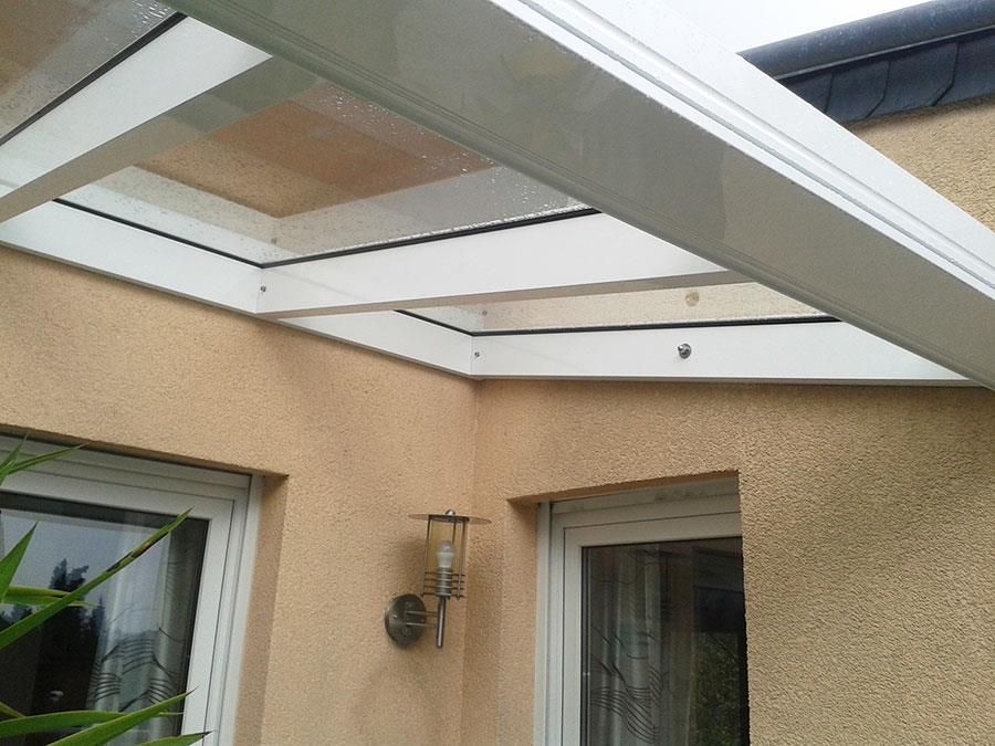 An der Seite eines Hauses befindet sich ein weißes Vordach mit einem Dach aus klarem Glas.