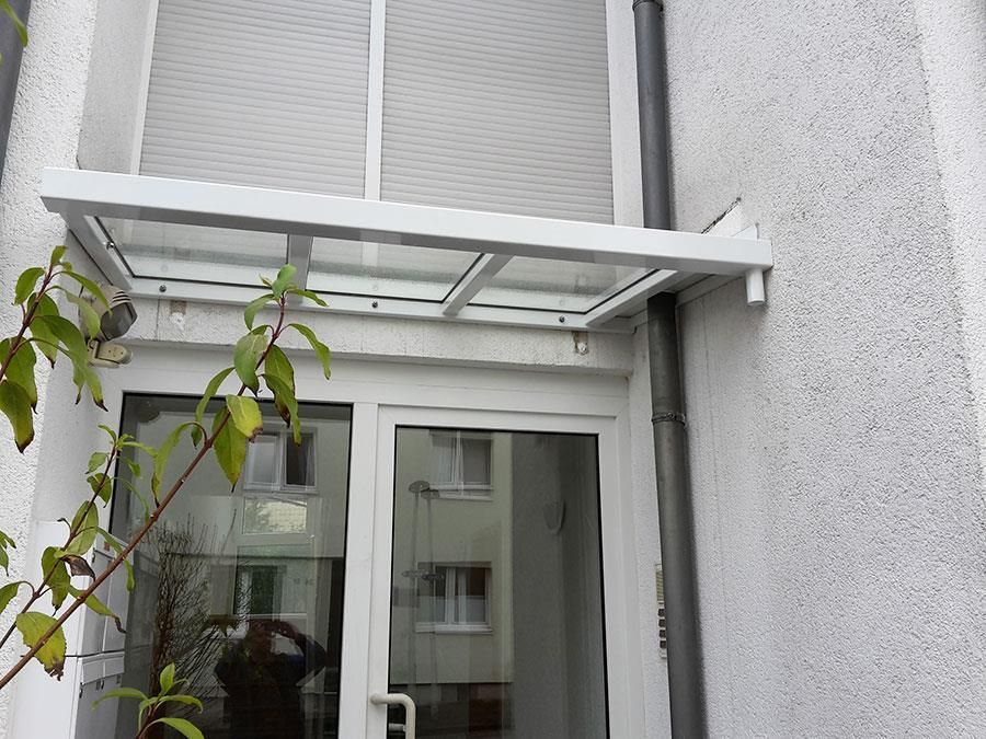 Ein weißes Gebäude mit einer Glastür und einem Vordach darüber.