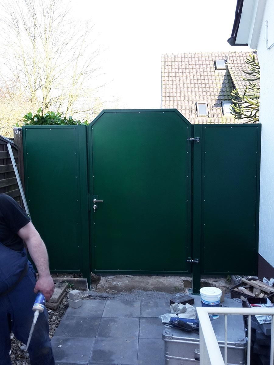 Ein Mann steht mit einem Schlauch vor einem grünen Tor.