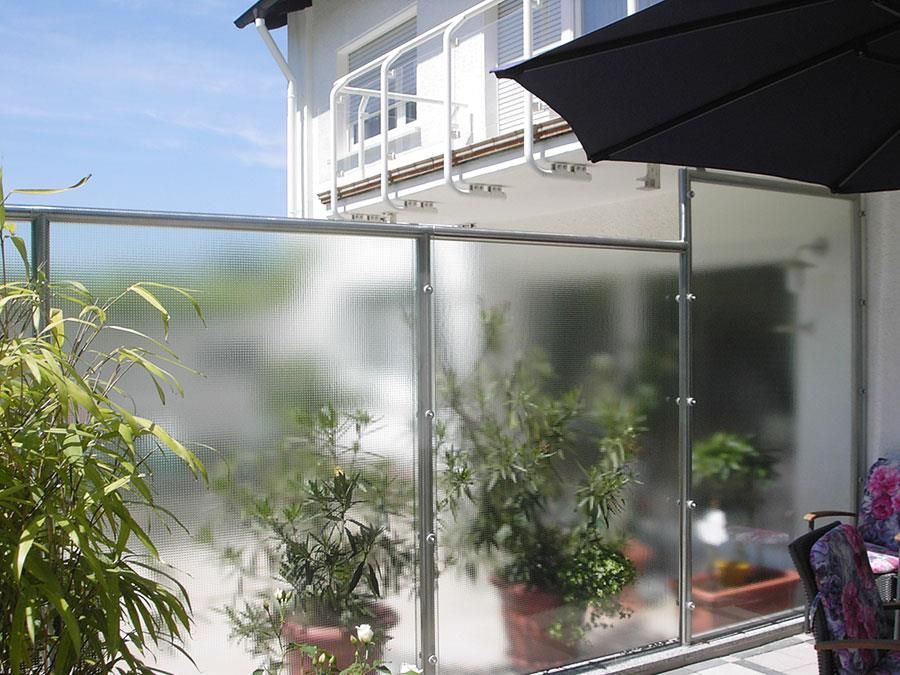 Ein Balkon mit Glasgeländer und schwarzem Sonnenschirm.