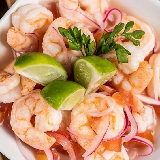 Un tazón de camarones, cebollas, tomates y rodajas de lima.