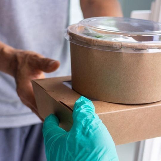 Una persona que lleva guantes verdes sostiene una caja de comida.