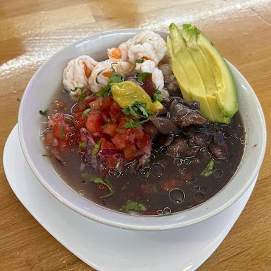 Un tazón de comida con aguacate, camarones, tomates y frijoles negros sobre una mesa.