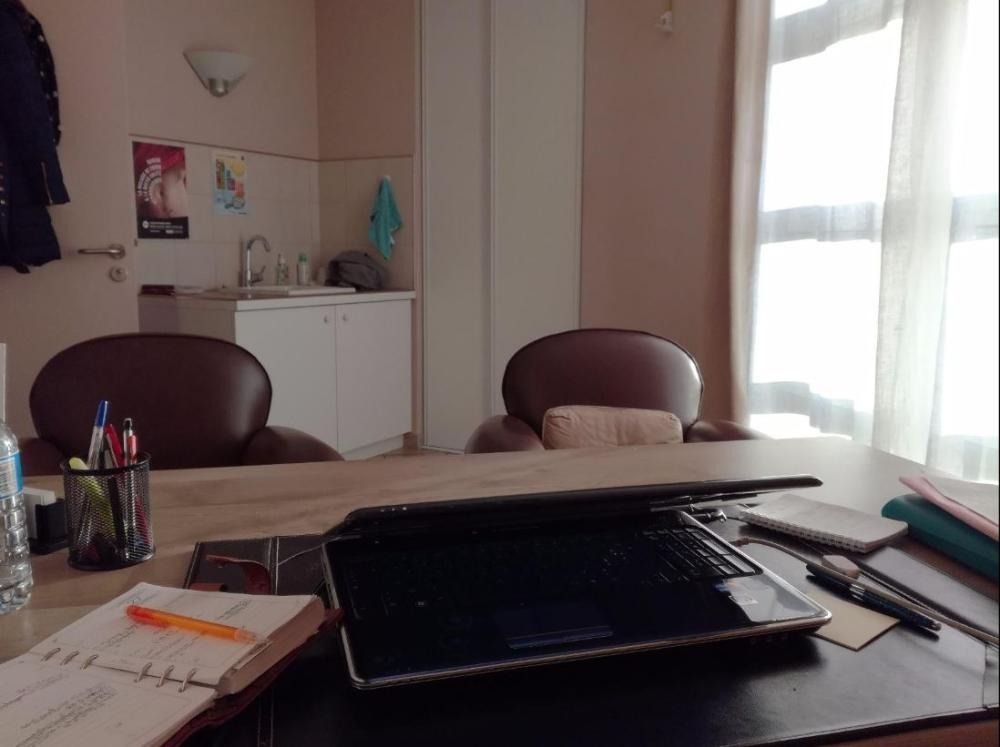 Bureau à domicile avec un ordinateur portable, des papiers, des stylos et des chaises près d’une fenêtre ornée de rideaux fins