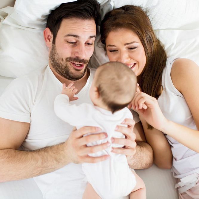 Ein Mann und eine Frau liegen auf einem Bett und halten ein Baby