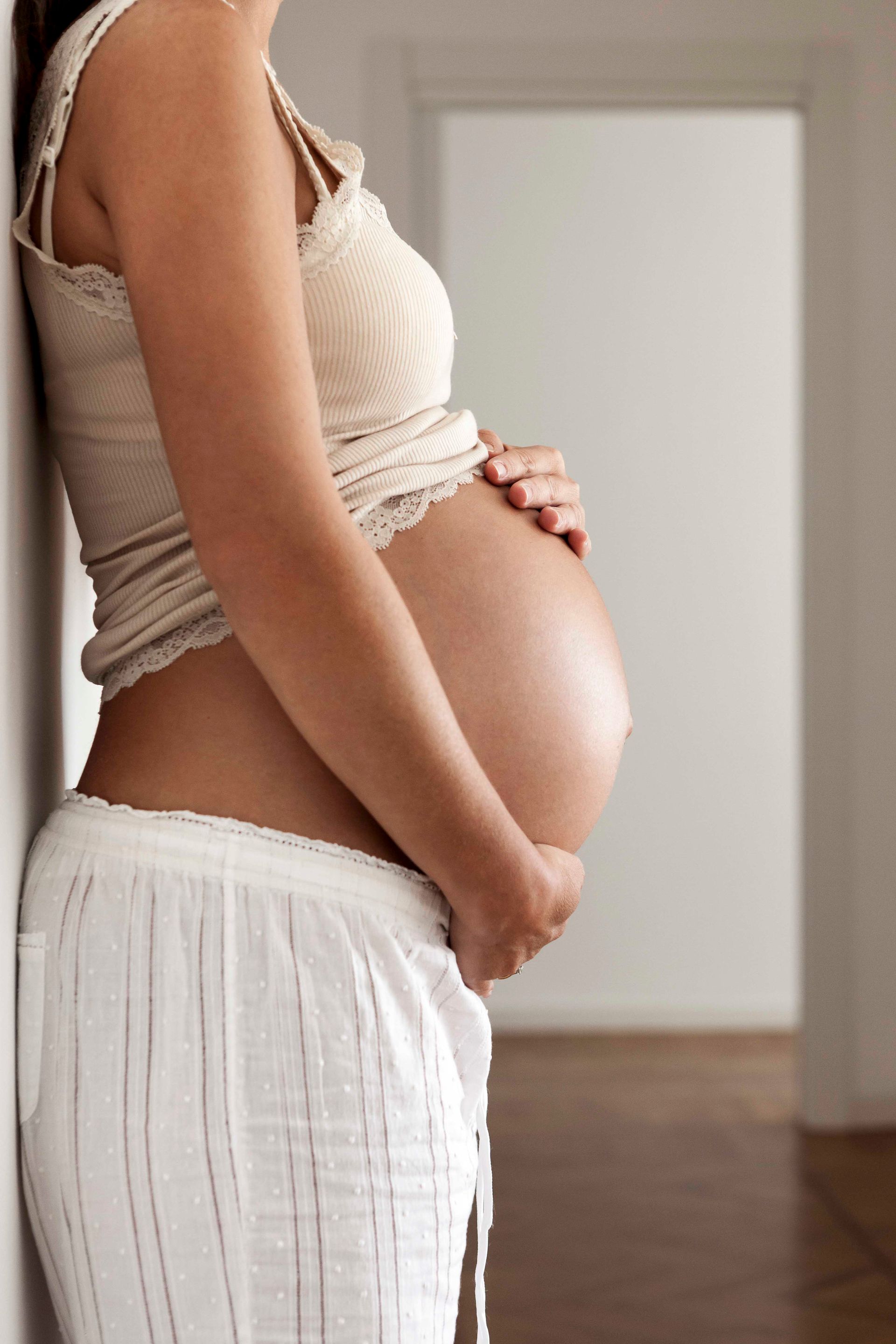 Eine schwangere Frau lehnt an einer Wand und hält ihren Bauch.