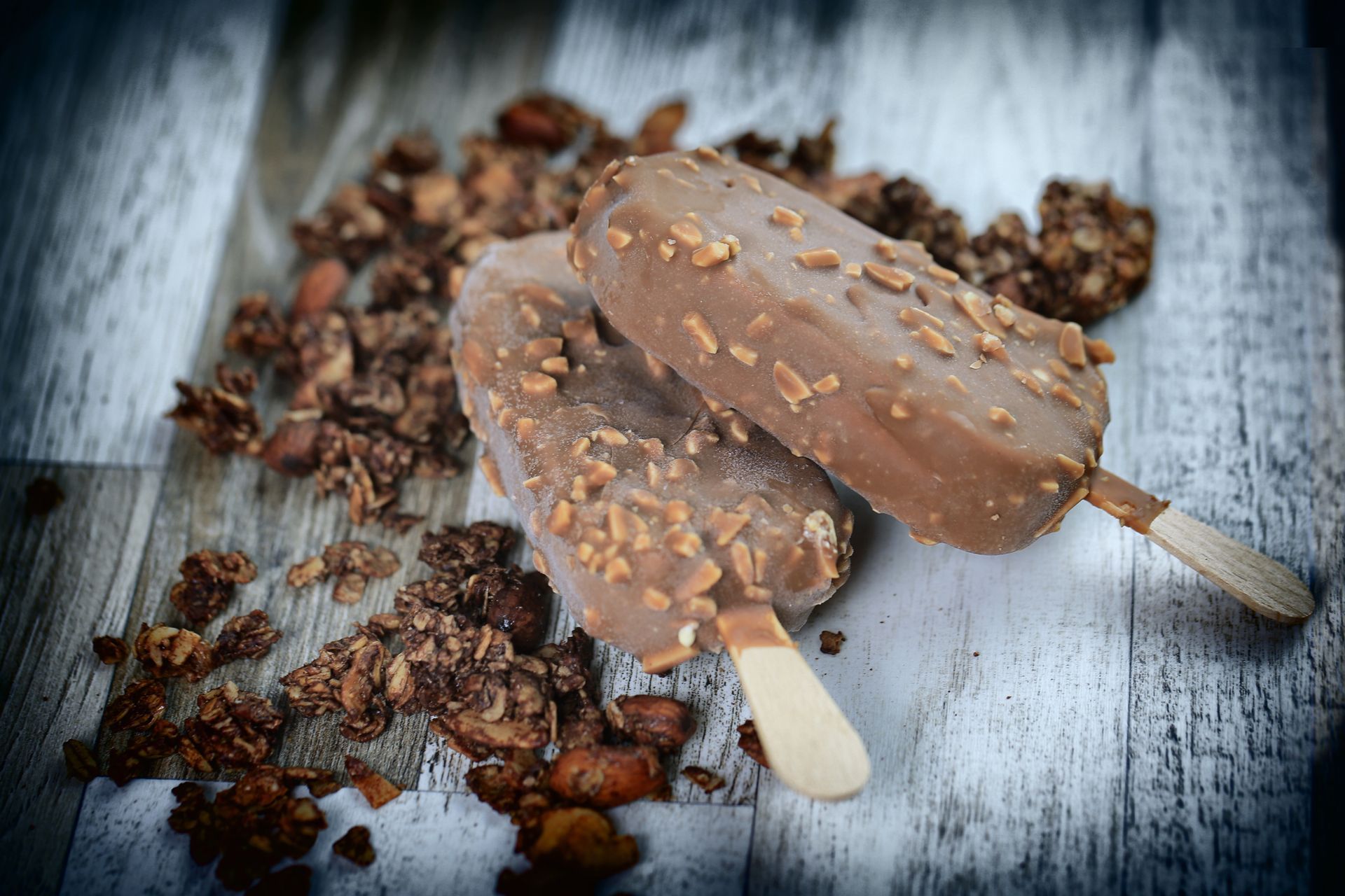 Deux barres glacées enrobées de chocolat avec des morceaux d'amandes, présentées sur une surface en bois avec du granola.