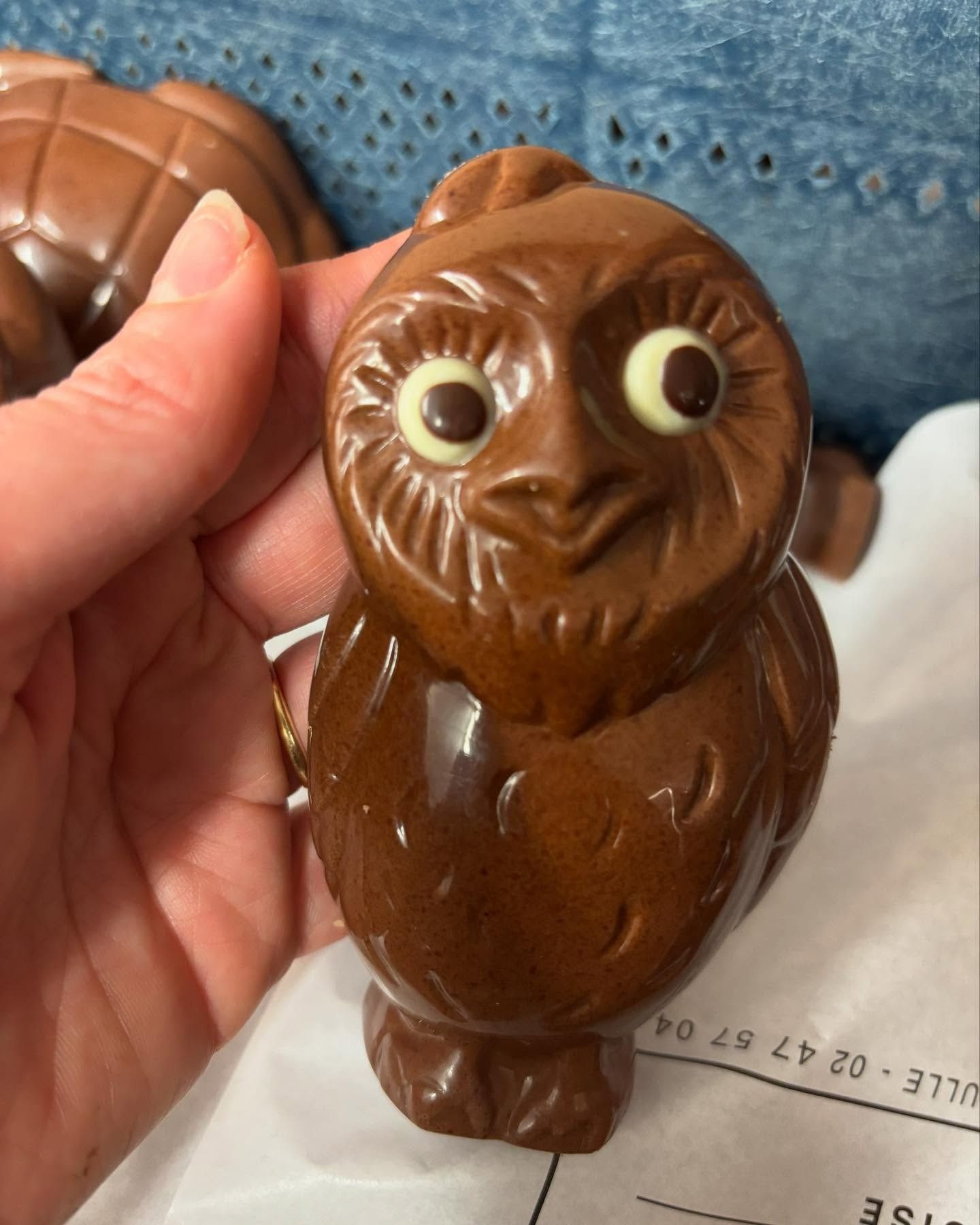 Figurine de hibou en chocolat aux yeux cerclés de blanc, tenue par une personne.
