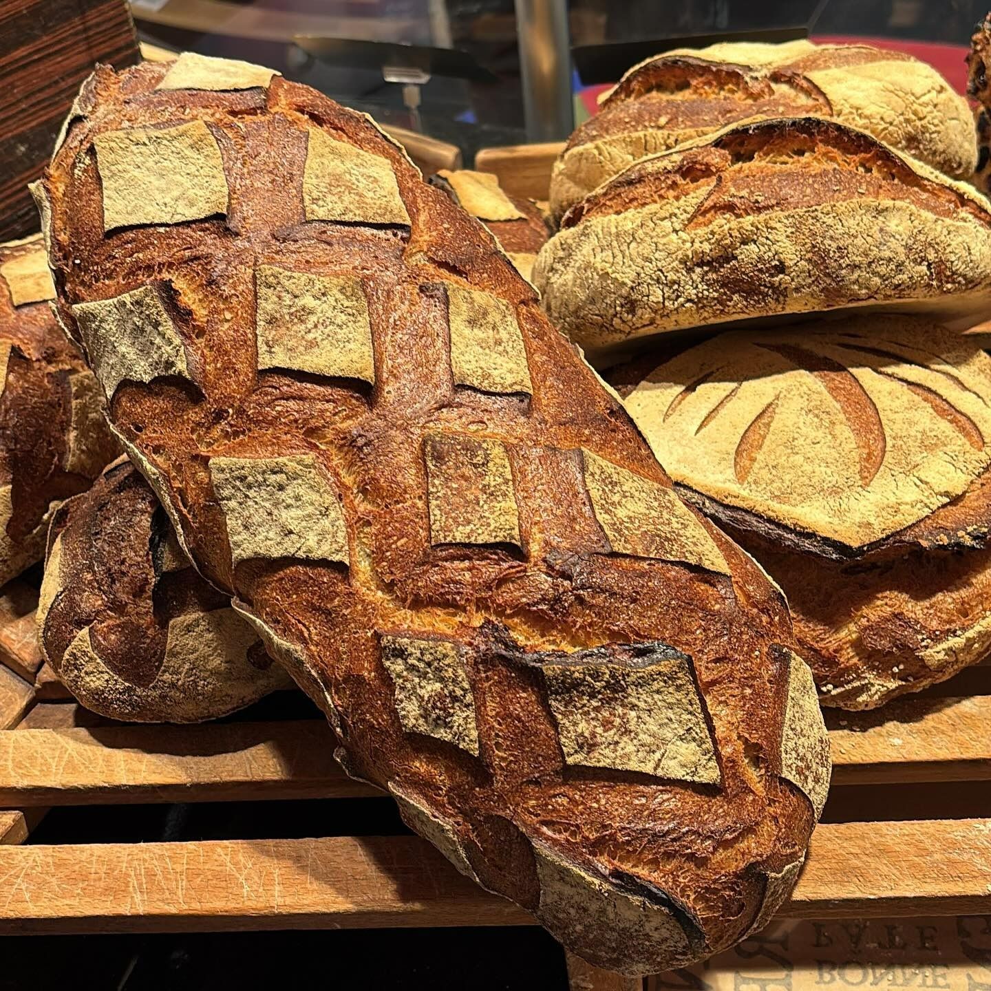 Présentation de miches de pain rustiques à croûte incisée, posées sur des lattes de bois.