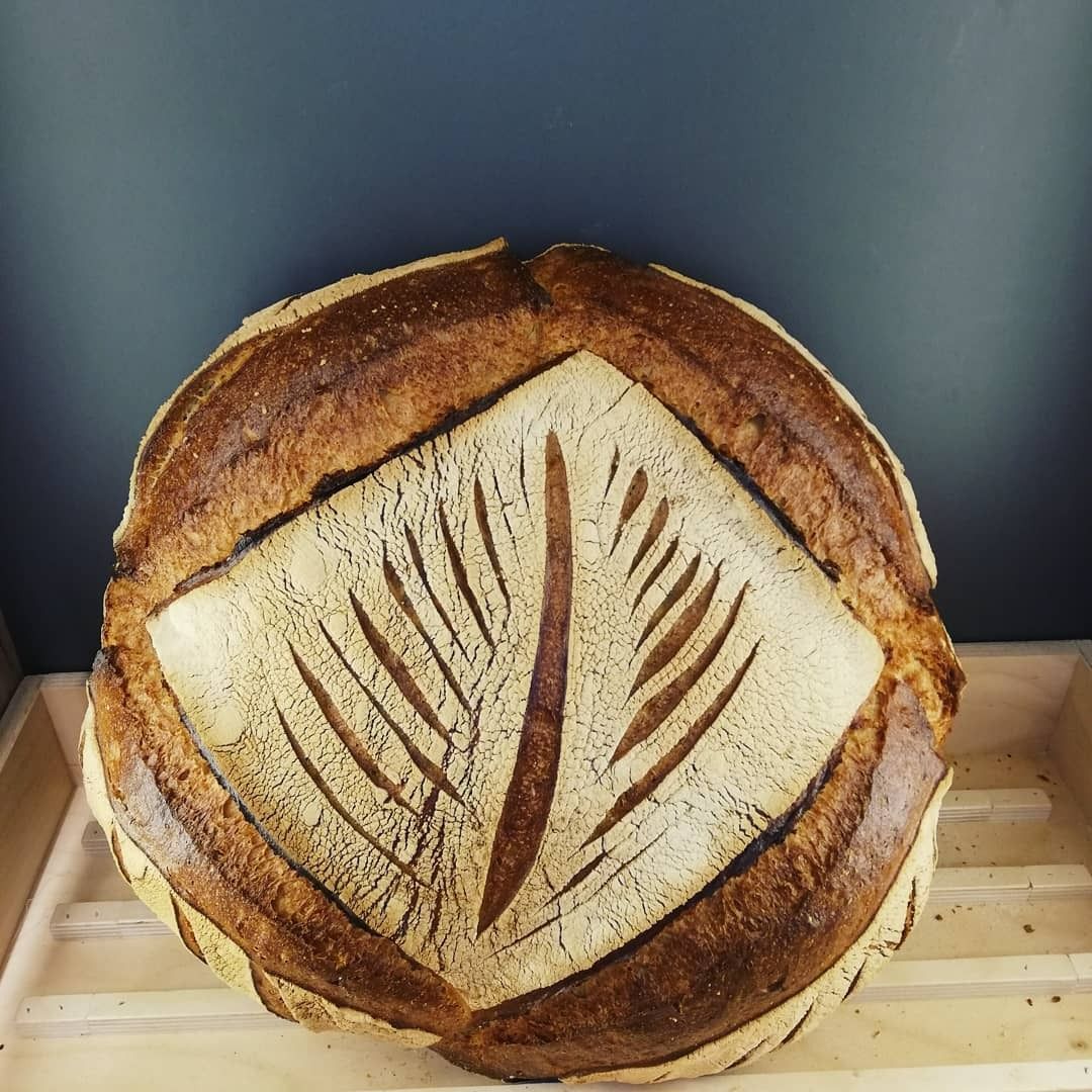 Pain rond décoré d'incrustations en forme de feuilles, présenté dans un plateau en bois.