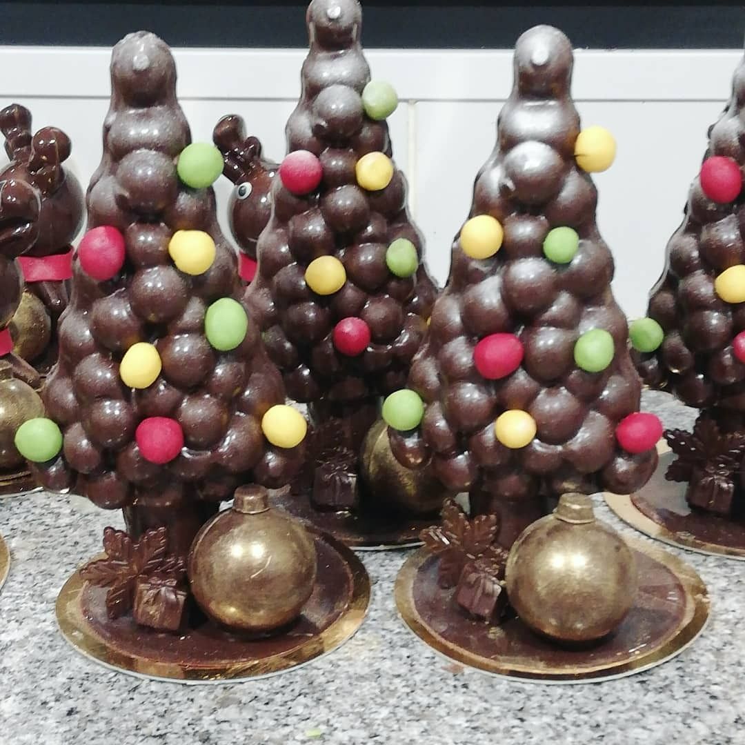 Sapins de Noël en chocolat décorés de bonbons colorés et de décorations dorées.