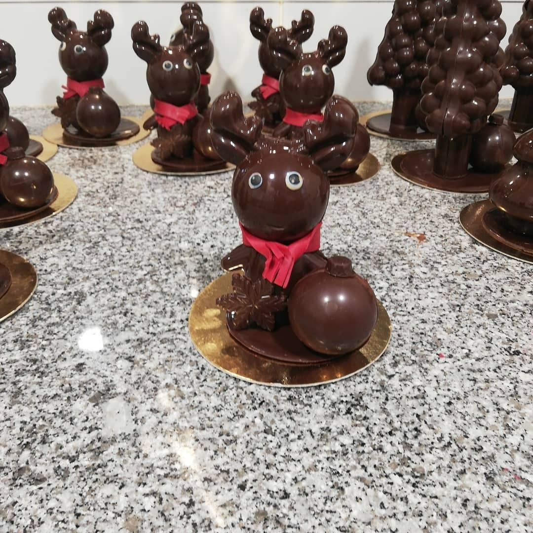 Des rennes en chocolat avec des écharpes rouges sont posés sur des assiettes dorées, exposés sur un comptoir.