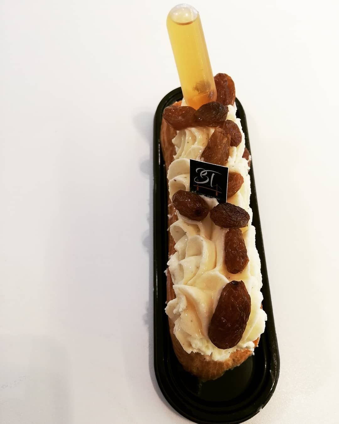 Éclair fourré à la crème, aux raisins secs et au miel, présenté sur un plateau noir.