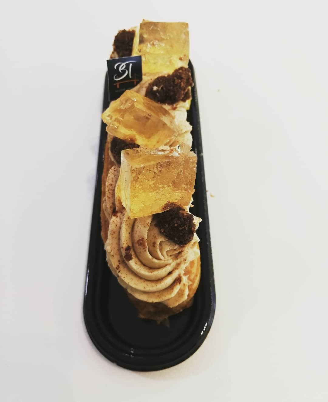 Éclair en boîte plastique noire, garni de crème, de morceaux de pâte et d'un drapeau de marque.
