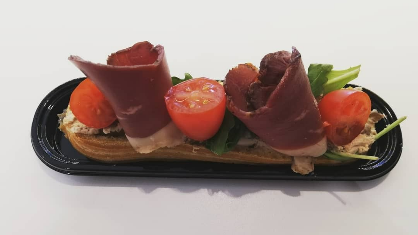 Éclair garni de rouleaux de viande, de tomates et de verdure, présenté sur un plat noir.