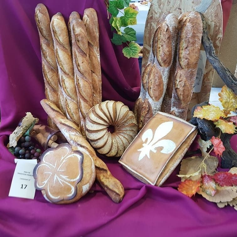 Présentation de différents pains sur une nappe violette, ornée de feuilles décoratives et d'une fleur de lys.