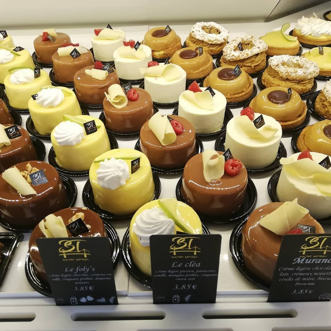Présentation de divers petits gâteaux glacés sur des assiettes noires dans une vitrine de boulangerie.