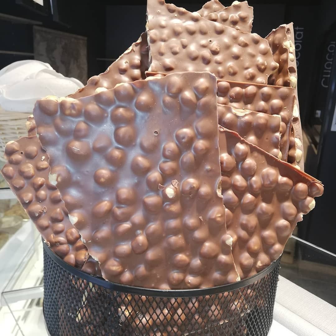 Écorce de chocolat parsemée de noisettes, présentée dans un panier en fil de fer noir.