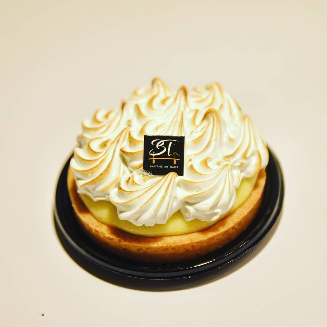 Tarte au citron meringuée sur un plateau noir, garnie de meringue grillée et d'un logo.