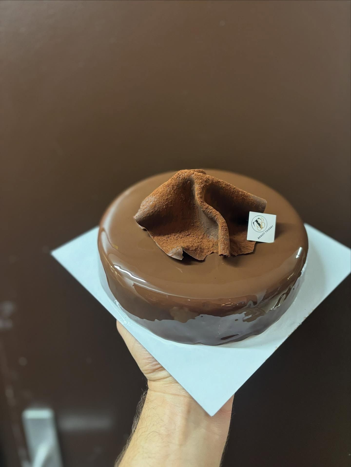 Main tenant un petit gâteau au chocolat avec un glaçage brillant, de la poudre de cacao et un tourbillon décoratif en chocolat.