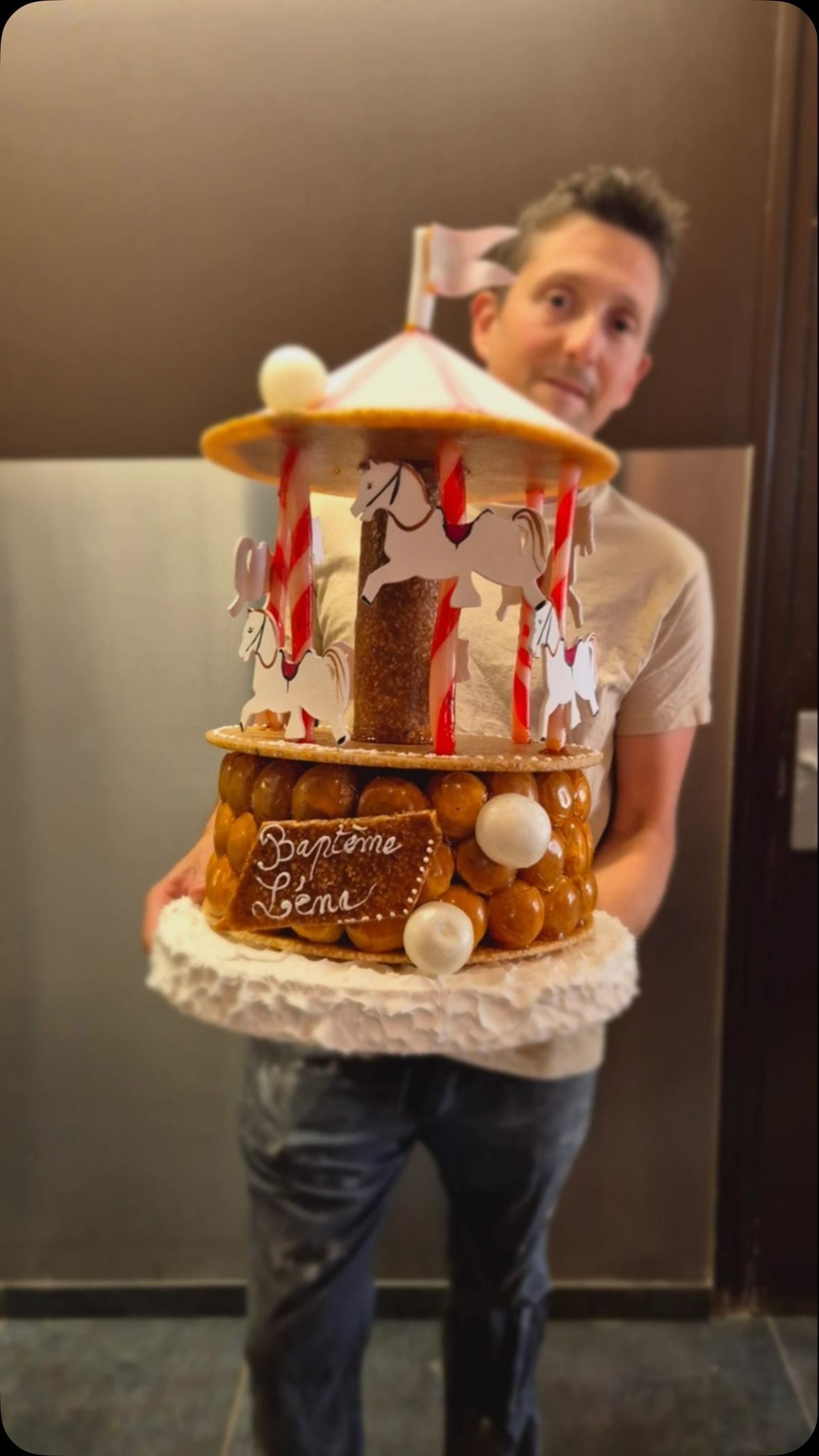 Un homme tient une pièce montée en forme de carrousel avec des chevaux blancs et des rayures rouges.