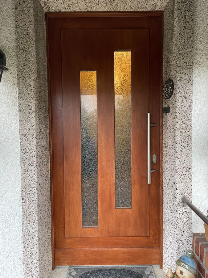 Eine Holztür mit zwei Fenstern an einer weißen Wand.