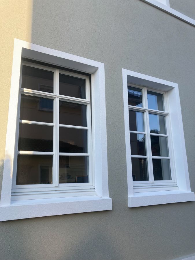 Zwei Fenster an der Seite eines Gebäudes mit weißen Zierleisten