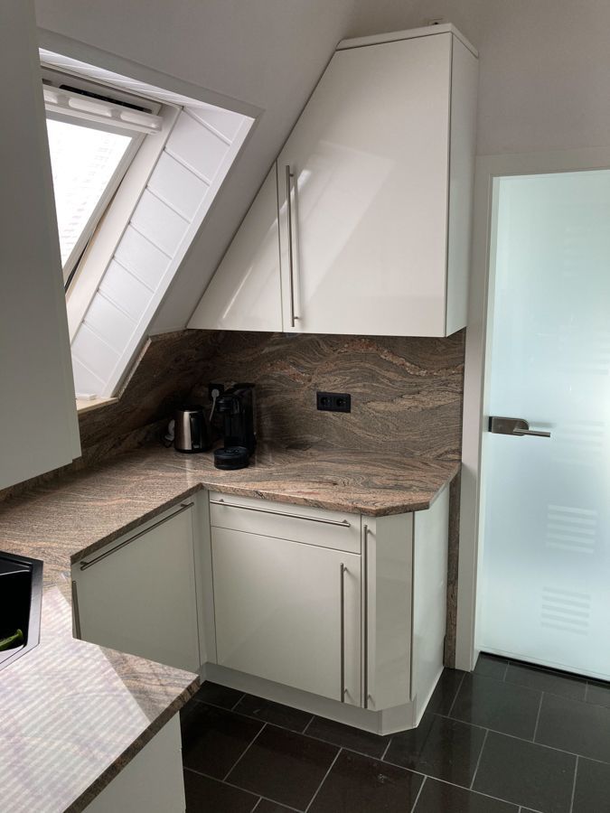 Eine Küche mit weißen Schränken und einer Glastür.